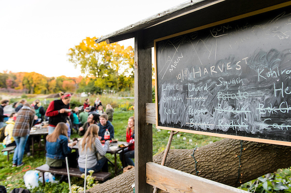 A chalkboard displays different types of produce harvested from the gardens, while students enjoy a meal together in the background.