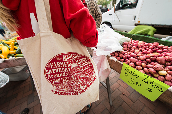 A shopper at the Dane County Farmers Market with a bag showing the Capitol and the text, "Madison, Wisconsin".
