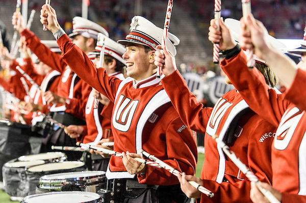 A row of drummers in marching band uniform smile to the crowd.