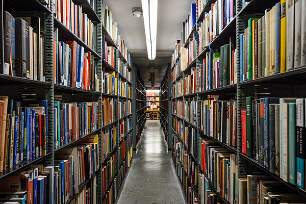 Rows and rows of books frame a corridor, with a student sitting at a desk at the end.