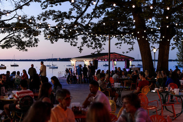 People sit around tables with the lake and sunset in the background.