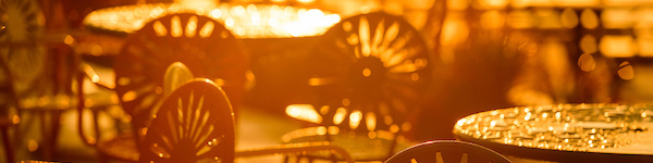 Tables and chairs outdoords at the terrace, covered with rain, take on an orange hue in the sunset after a storm.