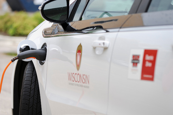 A clean, white car with the Wisconsin logo on the side is plugged in to charge.