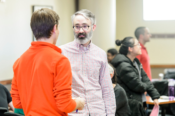 Two students stand in a classroom having a conversation.