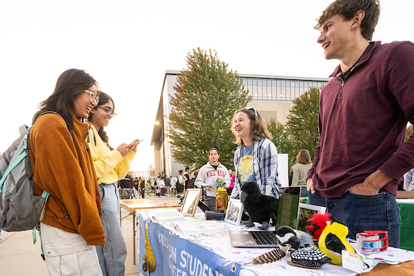 Two people stand behind a table with a banner and small display items of birds while talking and smiling with two visitors to their booth.