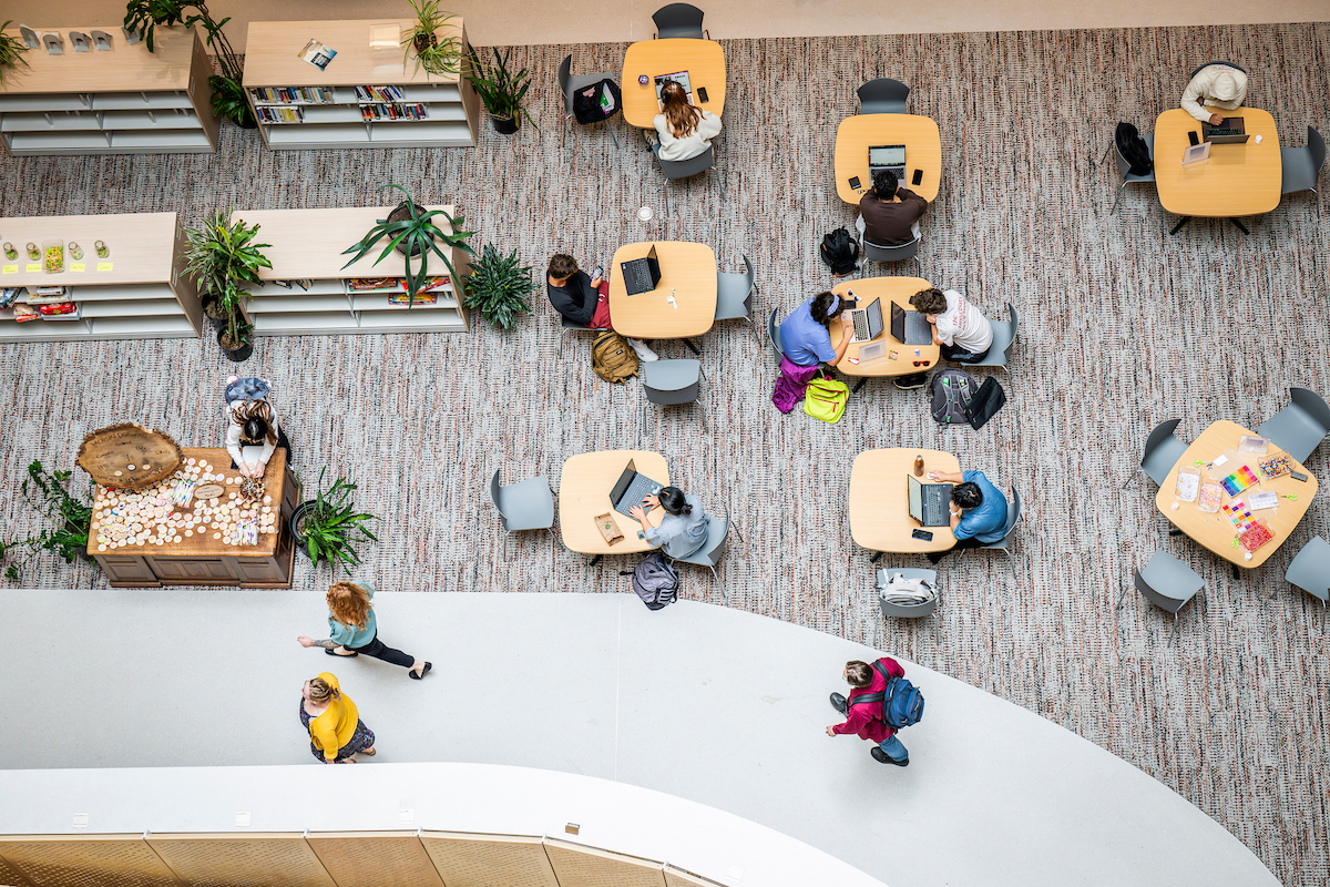 Aerial view of students seated at tables with their notebooks and laptops in front of them.