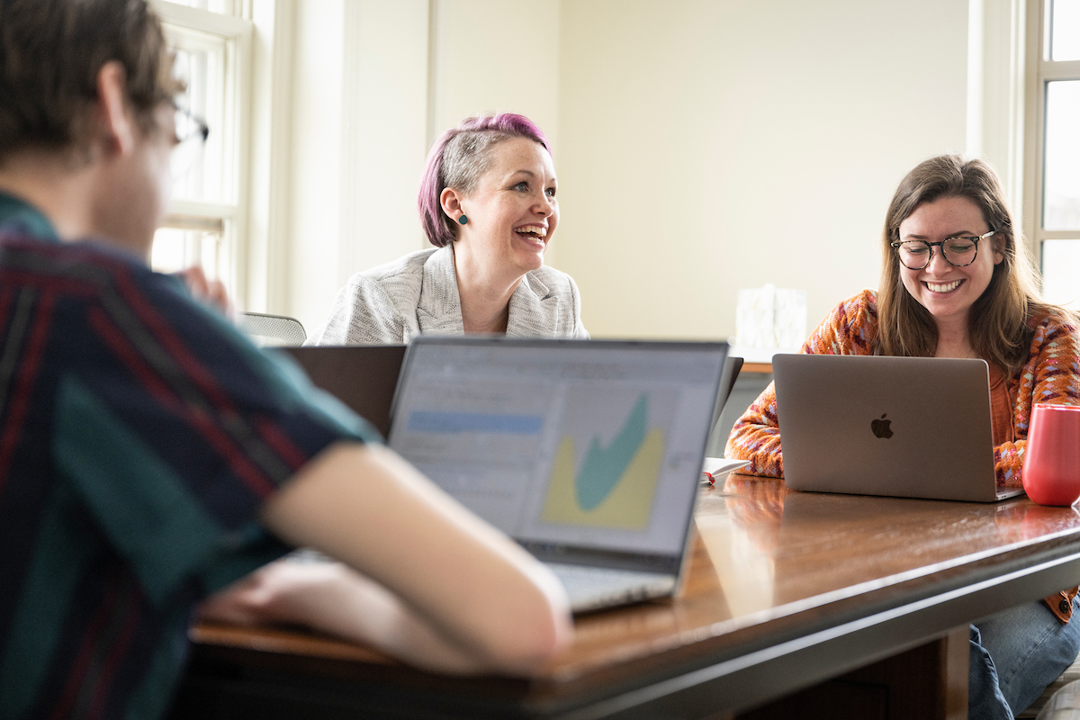 People around a meeting table smile during conversation.